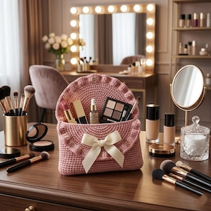 May include: A pink crocheted makeup bag with a cream-colored bow, filled with cosmetics. The bag is open, revealing lipsticks, eyeshadow, and other beauty products. Makeup brushes and other beauty items are arranged on a wooden surface.