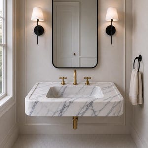 May include: A wall-mounted white marble sink with grey veining, featuring a brass faucet and two matching brass handles. Above the sink is a rectangular mirror with a black frame, flanked by two black wall sconces with white pleated shades.