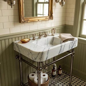 May include: A white marble sink with grey veining sits on a metal console stand. The sink features a chrome faucet, a soap dish with a bar of soap, and a textured beige towel. Below, a woven basket holds toilet paper rolls and glass bottles.