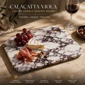 Puede incluir: Una tabla de servir rectangular de mármol Calacatta Viola con asa. La tabla tiene una base blanca con vetas moradas oscuras. Uvas, queso, prosciutto y nueces están dispuestos en la tabla. Una copa de vino tinto y un cuenco pequeño de nueces están en el fondo.