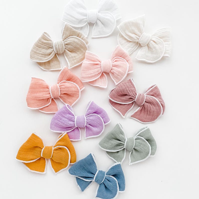 May include: A set of ten fabric hair bows with white trim. The bows are in various colors, including pink, purple, blue, green, and orange.