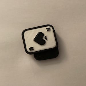 Può includere: Una spilla a forma di carta As di Picche in bianco e nero. La spilla presenta uno sfondo bianco con un simbolo di picche nero e la lettera "A". I bordi sono neri.