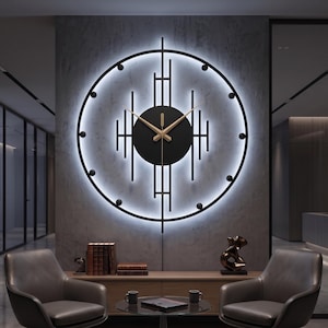 Könnte beinhalten: Eine große, kreisförmige Wanduhr mit einem schwarzen Metallrahmen, vertikalen geometrischen Stäben, einem zentralen schwarzen Zifferblatt und goldfarbenen Zeigern. Die Uhr wird durch eine weiße LED-Hintergrundbeleuchtung hell beleuchtet.