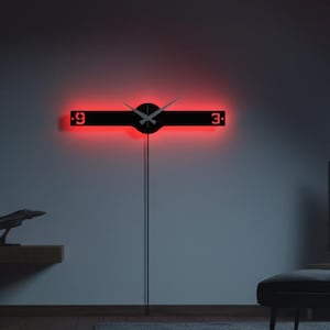 Könnte beinhalten: Eine horizontale schwarze Wanduhr mit roter LED-Hintergrundbeleuchtung, die über eine zentrale kreisförmige Nabe mit zwei Zeigern verfügt, wobei die Zahlen 9 und 3 auf beiden Seiten angezeigt werden. Die Uhr ist an einer Wand montiert.