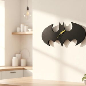 Könnte beinhalten: Eine schwarze Wanduhr in Form einer Fledermaus-Silhouette. Die Uhr hat eine mattschwarze Oberfläche mit leuchtend gelben Stunden-, Minuten- und Sekundenzeigern in der Mitte. Das Design ist flach und breit und erinnert an ein Comic-Emblem.