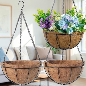 May include: Three hanging flower baskets with black metal frames and chains. The baskets have a brown, natural fiber lining. One basket is filled with colorful artificial flowers, including purple, blue, and white blooms. The other two baskets are empty.