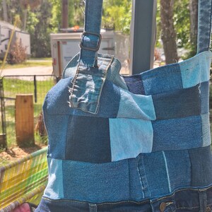 May include: A denim shoulder bag, crafted from patches of blue denim in various shades. The bag features a strap with a buckle and incorporates the waistband and pockets of a pair of jeans at the base. The bag is a unique, upcycled design.