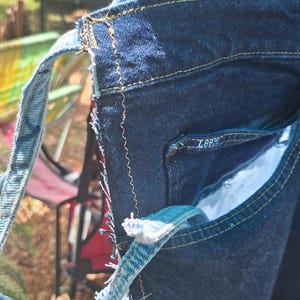 May include: Close-up of a denim bag with a patchwork design. The bag features various shades of blue denim, with visible stitching in yellow thread. The bag has a strap made from a lighter blue denim material. The Lee logo is visible on the pocket.