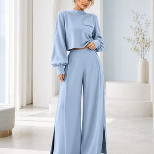 Puede incluir: Un conjunto de dos piezas azul claro que consta de un top corto de manga larga con cuello alto, un bolsillo en el pecho y pu&ntilde;os fruncidos, combinado con pantalones de cintura alta y pernera ancha con aberturas laterales en el bajo.