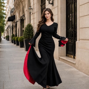 May include: A floor-length black dress with long sleeves featuring flared cuffs that reveal a vibrant red lining. The garment has a V-neckline, a fitted bodice, and a flared skirt that creates a distinct silhouette with a bold red interior contrast.