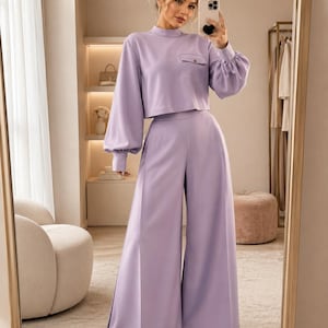 Puede incluir: Un conjunto de dos piezas en color lavanda que consta de una blusa corta de manga larga con cuello alto, un bolsillo en el pecho con bot&oacute;n y mangas voluminosas con pu&ntilde;os, combinado con pantalones de pierna ancha y cintura alta a juego.