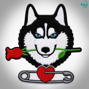 Puede incluir: Un parche bordado que muestra la cabeza de un perro husky en blanco y negro con ojos azul brillante. El perro sostiene una rosa roja en la boca. Debajo de la cabeza del perro hay un imperdible plateado con un corazón rojo en el centro.