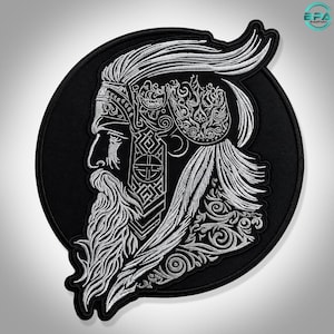 May include: A circular black embroidered patch featuring a detailed silver-toned profile of a bearded figure with long flowing hair. The design incorporates intricate knotwork patterns and decorative scrollwork elements throughout the hair and headgear.