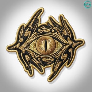 Puede incluir: Un parche bordado que presenta un ojo central con pupila vertical, representado en tonos dorados y negros. El diseño incluye patrones intrincados, arremolinados y puntiagudos que rodean el ojo, todo delineado con un borde dorado grueso.