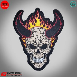 May include: Embroidered patch featuring a detailed skull with large horns and flames. The skull is off-white with black eyes and a wide grin. The horns are black with a pink outline, and the flames are yellow and orange. The patch has a black border.
