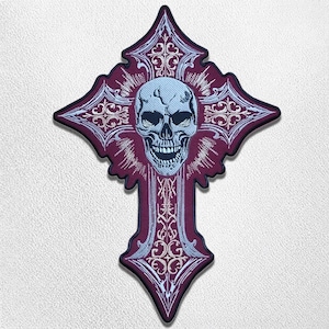 Puede incluir: Un parche bordado en forma de cruz que presenta una calavera central de color azul claro rodeada de intrincados patrones de filigrana blancos sobre un fondo burdeos profundo, con un borde oscuro y diseño simétrico.