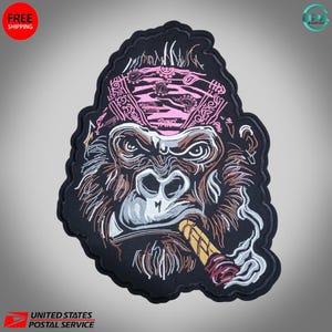 May include: Embroidered patch depicting a gorilla wearing a pink bandana and smoking a cigar. The gorilla has brown fur, white teeth, and a detailed design. The patch has a black border, suitable for clothing or accessories.