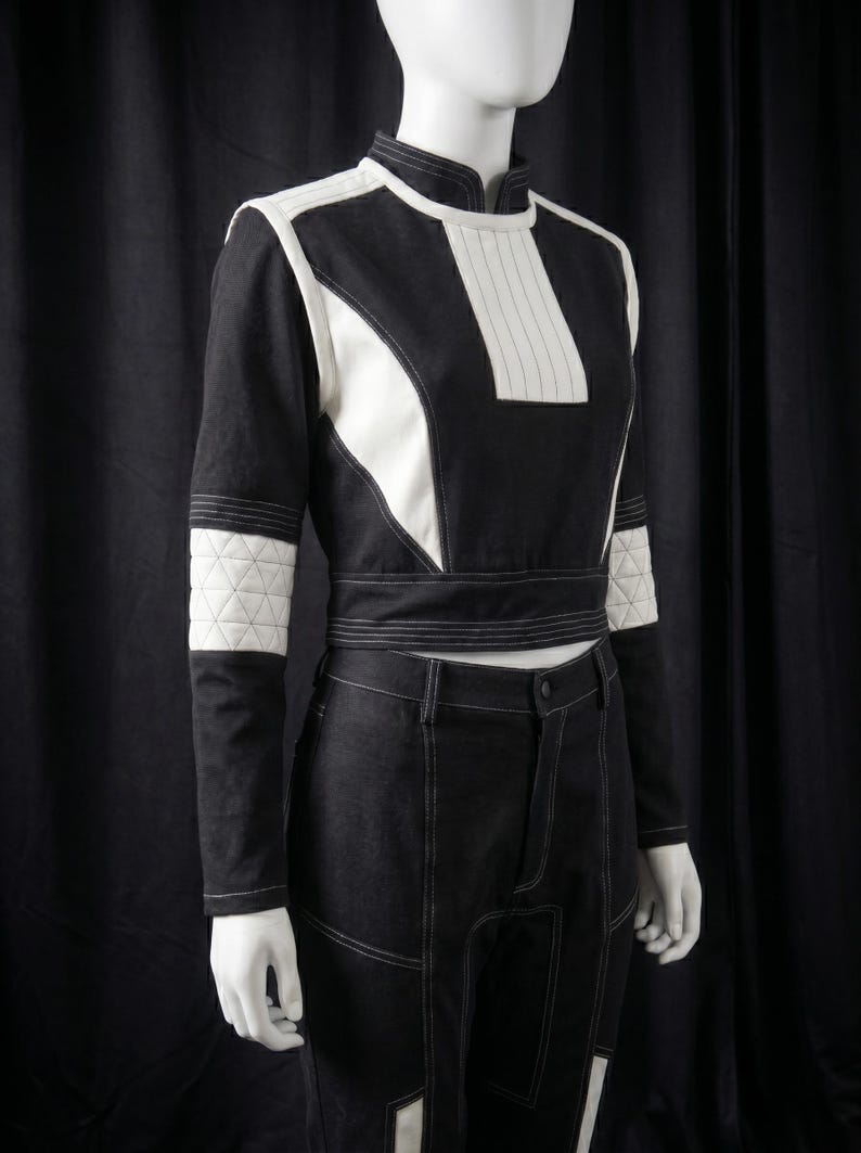 Puede incluir: Un conjunto de dos piezas en blanco y negro sobre un maniqu&iacute;. La parte superior tiene un cuello alto y detalles en blanco. Los pantalones son negros con costuras blancas. El conjunto tiene un dise&ntilde;o futurista.