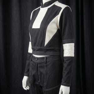 Puede incluir: Conjunto de dos piezas en blanco y negro, compuesto por un top corto y pantalones de cintura alta. El top presenta paneles blancos y una franja blanca vertical. Costuras blancas delinean el dise&ntilde;o. Mangas con parches blancos acolchados.