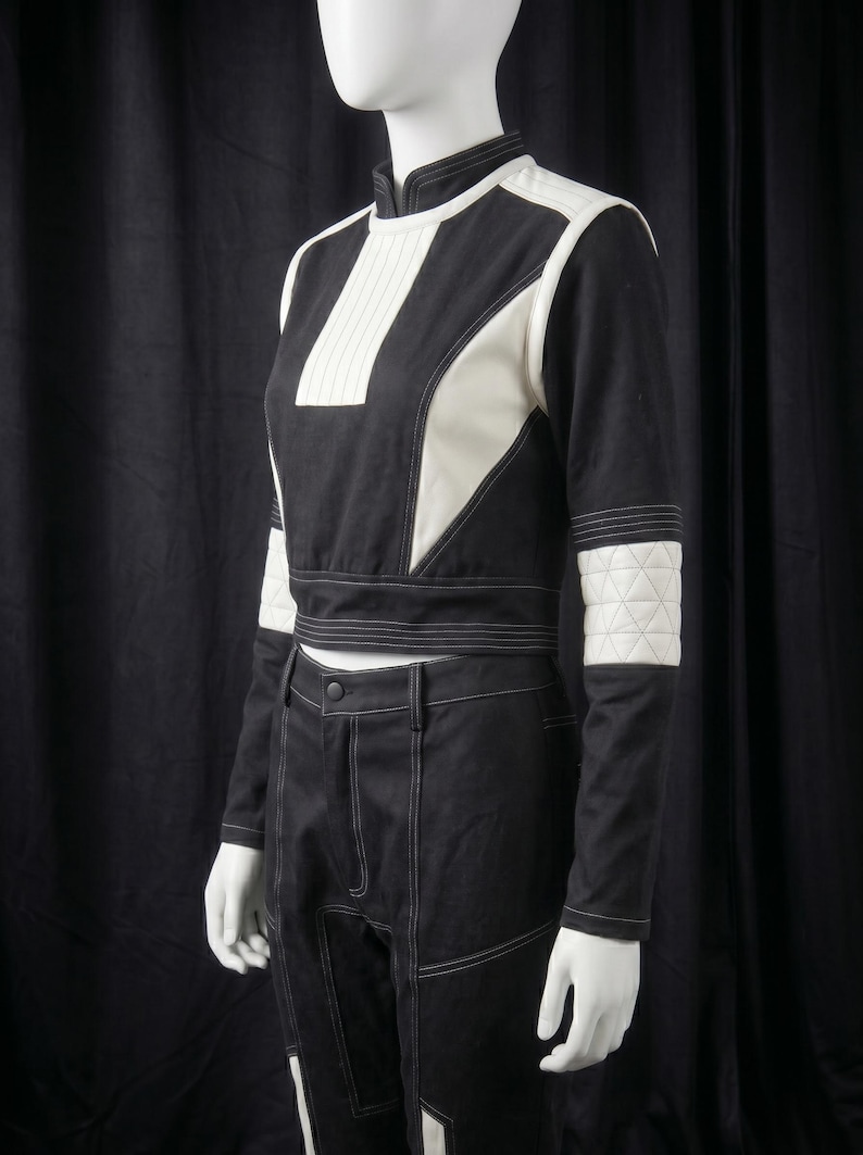 Puede incluir: Conjunto de dos piezas en blanco y negro, compuesto por un top corto y pantalones de cintura alta. El top presenta paneles blancos y una franja blanca vertical. Costuras blancas delinean el dise&ntilde;o. Mangas con parches blancos acolchados.