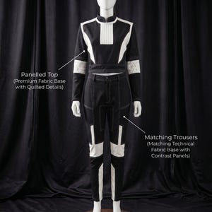 Puede incluir: Un disfraz en blanco y negro exhibido en un maniqu&iacute;. El disfraz incluye una parte superior con paneles y detalles acolchados y pantalones a juego con paneles en contraste. El texto "COSTUME INCLUDES" est&aacute; en la parte superior.