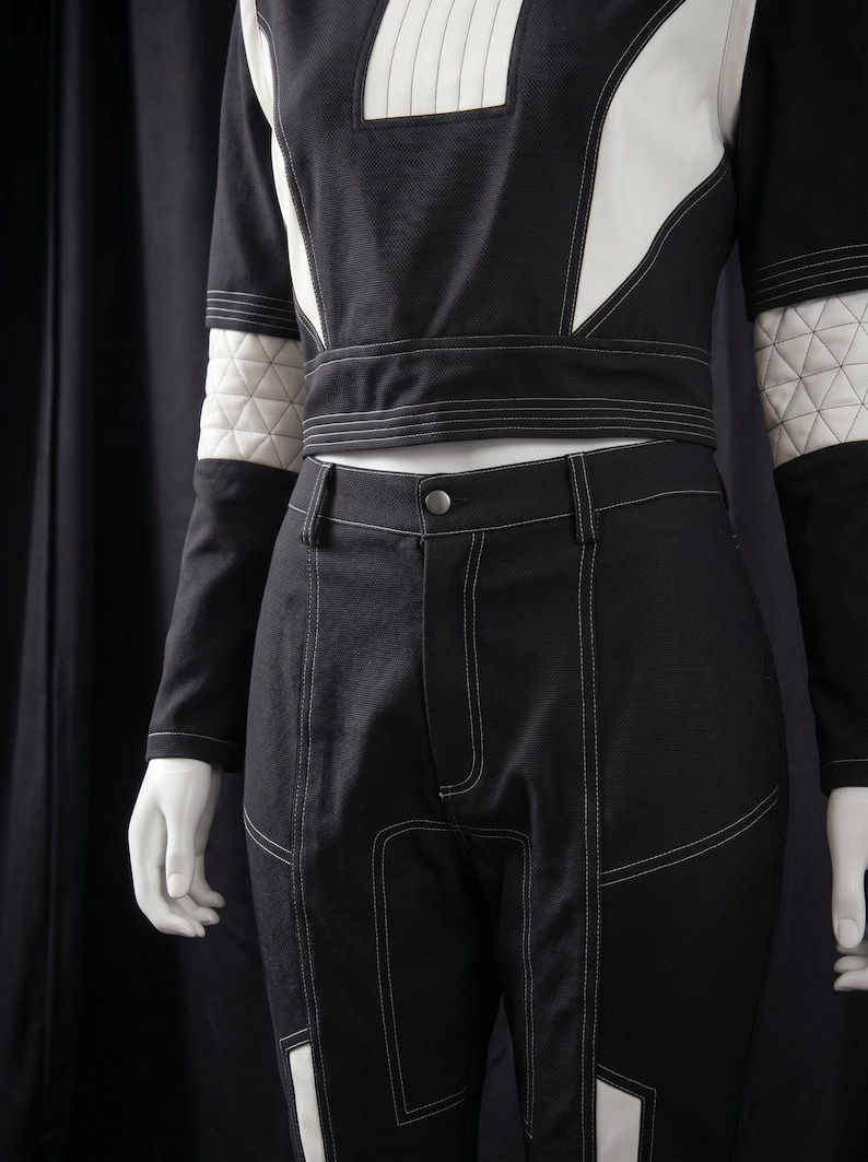 Puede incluir: Conjunto de dos piezas en blanco y negro. La parte superior tiene mangas largas con detalles acolchados blancos en la parte superior de los brazos. Los pantalones son negros con costuras blancas y paneles blancos. El conjunto se exhibe en un maniqu&iacute;.