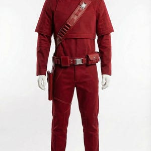 May include: A complete red costume displayed on a mannequin. The outfit includes a high-collared top, pants, belt with pouches, shoulder strap, and boots. The costume has a textured appearance and is likely made of a durable fabric.