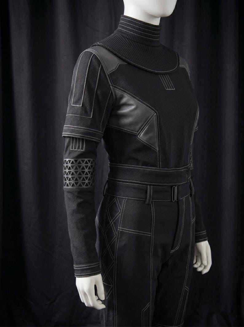 May include: Black jumpsuit with white stitching details. The outfit features a high collar, leather accents, and geometric patterns on the sleeves. The pants have a belt and a tailored fit, creating a futuristic or cosplay aesthetic.