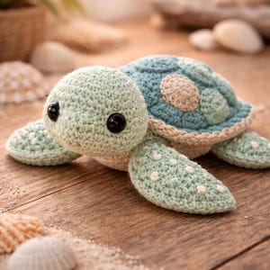 May include: A crocheted turtle toy in seafoam green, light blue, and beige. The turtle has large black eyes and white spots on its flippers. The toy is displayed on a wooden surface with seashells.