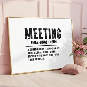 May include: A rectangular framed wall art piece featuring a white background with black text that reads: MEETING (MEE-TING) NOUN. A SCHEDULED INTERRUPTION OF YOUR ACTUAL WORK, OFTEN ENDING WITH MORE QUESTIONS THAN ANSWERS. The frame is thin and metallic gold.