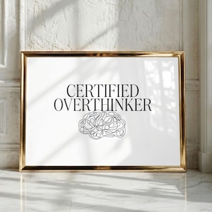 Pode incluir: Uma impressão de arte de parede retangular numa moldura dourada com o texto preto CERTIFIED OVERTHINKER centrado acima de um desenho de linha preta de um cérebro humano. O design está sobre um fundo branco liso, criando um contraste.