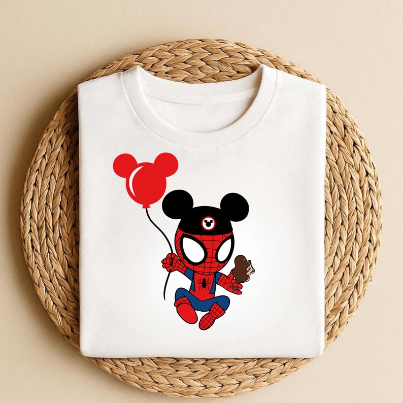 May include: White t-shirt featuring a cartoon character combining elements of Spider-Man and Mickey Mouse. The character holds a red balloon and a chocolate treat. The design is in red, blue, black, and white.