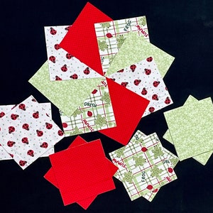 May include: A collection of nine fabric squares with various patterns and colors. The squares are made of green, red, and white fabric with a variety of designs including ladybugs, frogs, and plaid. The squares are arranged in a starburst pattern.