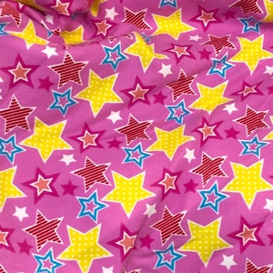 May include: Pink fabric with a repeating pattern of yellow, red, blue, and white stars. The stars have different patterns, including polka dots, stripes, and solid colors.