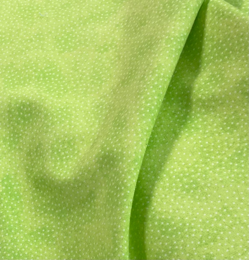 May include: A close-up of a green fabric with a white polka dot pattern. The fabric is folded in half, showing the texture and pattern.