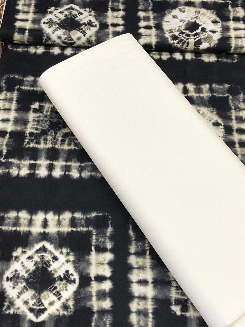 May include: A white fabric swatch laid on top of black fabric with a white and gray tie-dye pattern.
