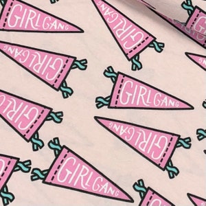 May include: Pink and white fabric with a repeating pattern of pink pennants with the text "GIRL GANG" in white. The pennants have a blue and white stitched border and blue and white tassels.
