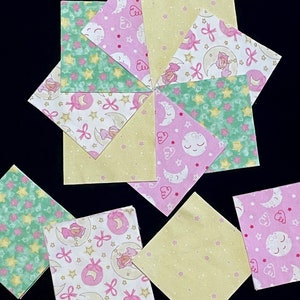 May include: A set of nine fabric squares with a variety of patterns featuring stars, moons, and bows in pink, green, and yellow.