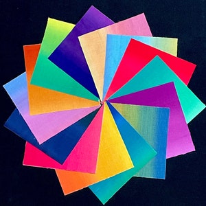 Könnte beinhalten: Eine Sammlung von 16 Stoffquadraten, die in einem Kreis angeordnet sind. Die Quadrate sind in verschiedenen Farben, darunter Rot, Orange, Gelb, Grün, Blau, Lila und Pink. Jedes Quadrat hat einen Farbverlauf, wobei der hellste Farbton in der Mitte und der dunkelste Farbton am Rand liegt.