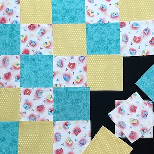 May include: A quilt block with a patchwork design featuring a repeating pattern of teddy bears in various colors. The quilt block is made up of nine squares, each with a different pattern. The squares are arranged in a grid pattern. The quilt block is made of fabric with a light blue, yellow, and white background.
