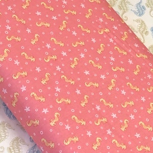 Op de afbeelding: Roze stof met een herhalend patroon van gele zeepaardjes, witte sterren en witte cirkels.