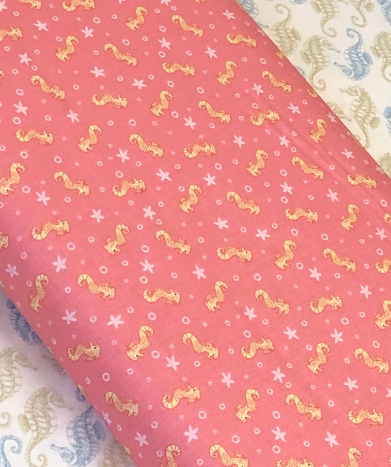 Op de afbeelding: Roze stof met een herhalend patroon van gele zeepaardjes, witte sterren en witte cirkels.