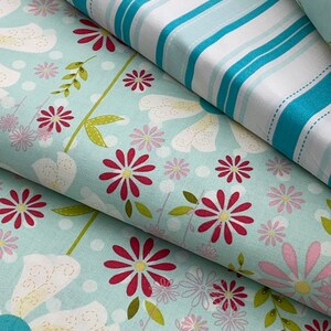 May include: Two fabric swatches, one with a blue and white striped pattern and the other with a light blue background and a floral pattern featuring red, pink, and white flowers.