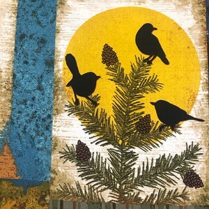 May include: A fabric panel featuring a nature scene with a yellow sun, black bird silhouettes, pine needles, and pine cones. The background includes blue, green, and brown textured patterns and a plaid design.