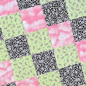 May include: A patchwork quilt featuring a range of patterns, including pink and white clouds, black and white floral, and green with white milk bottles and cows.