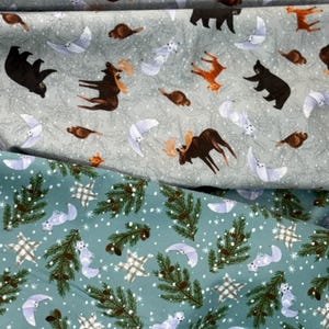 May include: Fabric with a repeating pattern of woodland animals, including bears, moose, foxes, and owls, in shades of brown, orange, and white on a light gray background. A second fabric layer features a teal background with pine branches, stars, and snow.
