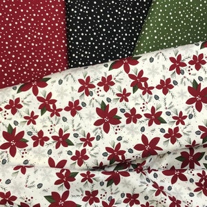 May include: A white fabric with a red poinsettia floral pattern. The fabric is folded over a black fabric with white polka dots and a green fabric with white polka dots.