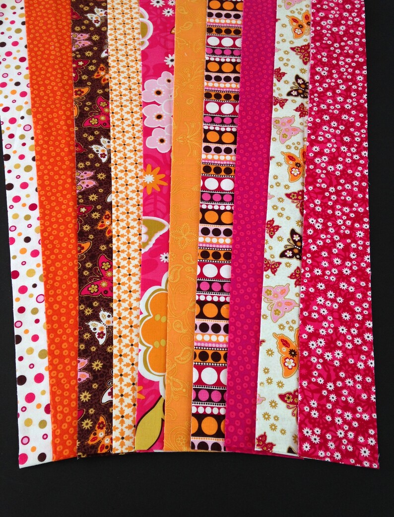 May include: Assortment of 10 fabric strips in various pink, orange, and brown patterns. The strips feature butterflies, polka dots, and floral designs.