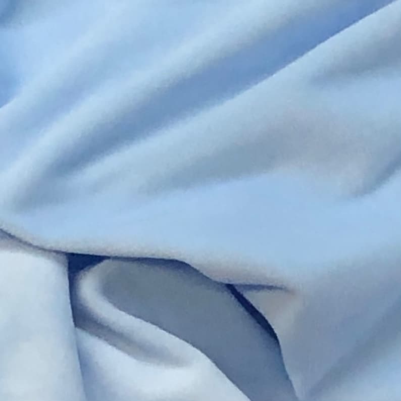 May include: A close-up of a light blue fabric with a soft, smooth texture. The fabric is folded and draped, creating a sense of movement and flow.
