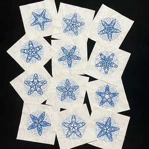 May include: Twelve white fabric squares with blue embroidered snowflake designs. Each square features a different snowflake design.